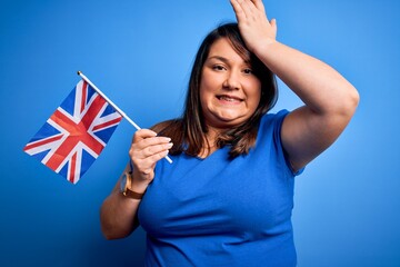 Beautiful plus size woman holding united kingdom flag over blue background stressed with hand on head, shocked with shame and surprise face, angry and frustrated. Fear and upset for mistake.