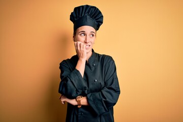 Young beautiful chef woman wearing cooker uniform and hat standing over yellow background looking stressed and nervous with hands on mouth biting nails. Anxiety problem.