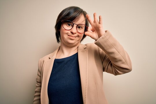 Young down syndrome business woman wearing glasses standing over isolated background smiling positive doing ok sign with hand and fingers. Successful expression.