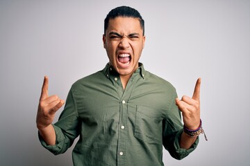Fototapeta premium Young brazilian man wearing casual shirt standing over isolated white background shouting with crazy expression doing rock symbol with hands up. Music star. Heavy concept.