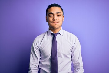 Young brazilian businessman wearing elegant tie standing over isolated purple background puffing cheeks with funny face. Mouth inflated with air, crazy expression.