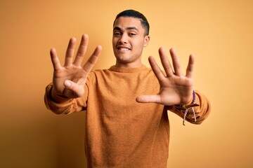 Young brazilian man wearing casual sweater standing over isolated yellow background showing and pointing up with fingers number nine while smiling confident and happy.