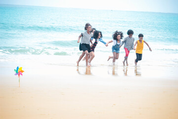 Group of six boys and girls holding hands in a line running on the beach, cute kids having fun on sandy summer beach, happy childhood friend playing on tropical sea