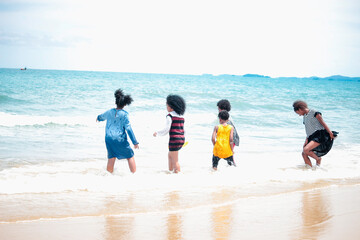 Fototapeta na wymiar Group of boys and girls running and makeing splashes in shallow sea water, cute kids having fun on sandy summer beach, happy childhood friend playing together on tropical beach