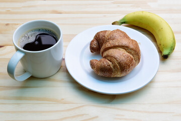 Breakfast with cup of coffee, americano coffee cup and fresh baked croissants with ripe yellow banana on wooden background on top view