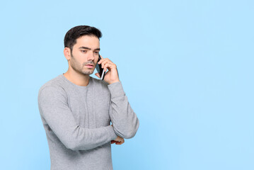 Portrait of serious handsome Caucasian man having conversation on phone in isolated studio blue...