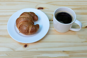 Morning coffee, americano coffee cup and fresh baked croissants on wooden background on top view.