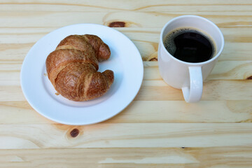 Morning coffee, americano coffee cup and fresh baked croissants on wooden background on top view.