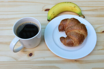 Breakfast with cup of coffee, americano coffee cup and fresh baked croissants with ripe yellow banana on wooden background on top view