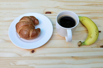 Breakfast with cup of coffee, americano coffee cup and fresh baked croissants with ripe yellow banana on wooden background on top view