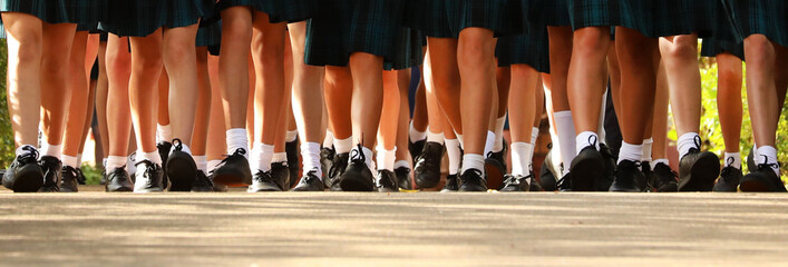 wide worms eye view multiple many female girls legs wearing school uniform of white socks black shoes and tartan skirt. Walking in together on the first day of high school.