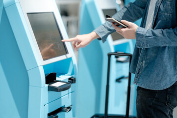 Male tourist holding passport and smartphone using self check-in kiosk in airport terminal. Travel...