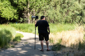 Photographer with large white lens on monopod walking on path in the woods looking for wildlife