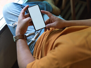 Male freelancer resting with mock-up smartphone while lying relaxed on office chair near window