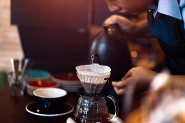 barista pouring boiling water from kettle to drip coffee maker.