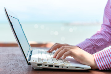 Woman hand using laptop to work study on work desk with clean nature beach outdoor background. Business, financial concept.