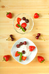 Ice cream dessert with strawberries and cherries in two plate on a wooden table. Copy space.