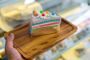 Naklejka na ściany i meble Piece of Rainbow Cake on wooden plate in shop