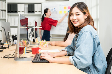 Portrait of smiling pretty young business asian woman working on computer desktop in modern workplace