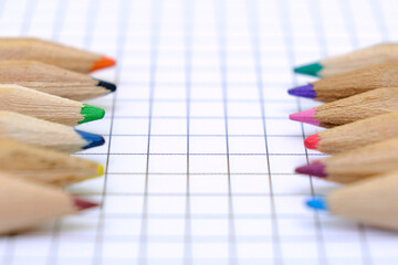 Obraz premium Closeup set of multicolored pencils on the checkered paper sheet of notebook for the drawing. Back to school concept.