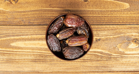 Dates in wooden bowl on wooden background.