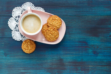 Oatmeal raisin nut cookie and pink cup of coffee with milk on wooden background