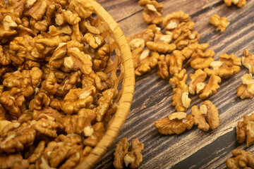 Peeled walnuts in a wicker basket and peeled walnuts scattered on a wooden table. Healthy diet. Fitness diet. Close up.