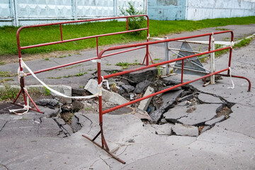 Broken mangled road and sewer hatch, fencing and hazard warning signs                               