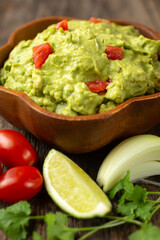 Fresh guacamole with tomato lime and coriander in a wooden bowl