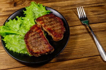 Grilled pork steaks with lettuce leaves on wooden table