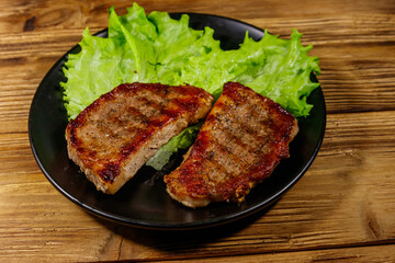 Grilled pork steaks with lettuce leaves on wooden table