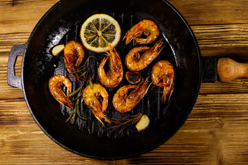 Grilled shrimp with spices, rosemary and lemon in a grill frying pan on a wooden table. Top view