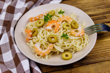 Spaghetti pasta with prawns, green olives and parsley on wooden table