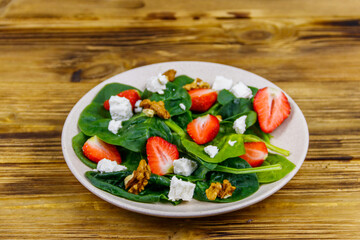 Fresh healthy salad with strawberry, spinach, walnuts and feta cheese on wooden table