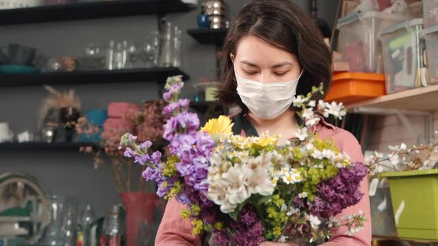asian woman in mask arranging bouquet. floral composition. Female florist making modern bouquet. of wildflowers chamomile. flower shop during flu illness pandemic