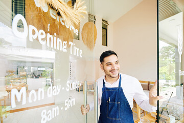 Excited happy young man opening door of his bakery shop and waiting for customers