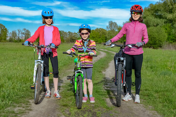 Happy mother and kids on bikes cycling outdoors in park, active family sport together
