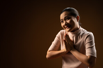 Asian woman guilty holding hands in prayer standing isolated on beige background. Low key.
