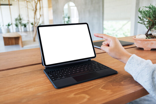 Mockup image of a woman using and pointing finger at tablet pc with blank desktop white screen as a computer pc on wooden table