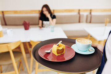 Waiter bringing tray with cup of coffee and sweet dessert to female customer, selective focus
