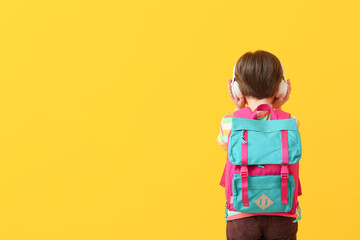 Cute little schoolboy listening to music on color background