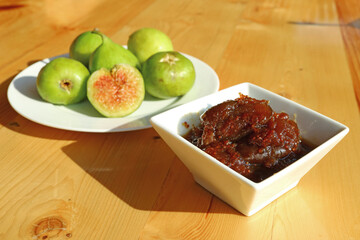 Tasty homemade fig jam with a plate of green fresh figs in the backdrop