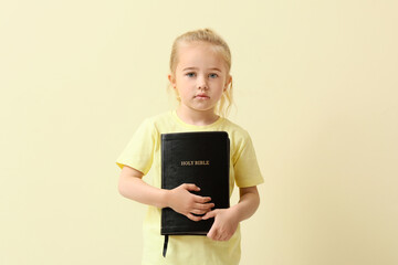 Little girl with Bible on color background