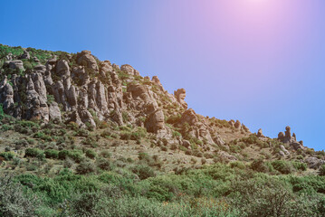 Mountain with green trees against a clear sky with sunbeams.
