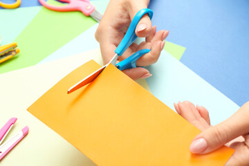 Woman with scissors cutting paper on color background