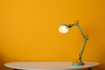 Glowing lamp on table near color wall