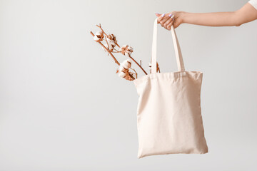 Female hand with cotton flowers and shopping bag on light background
