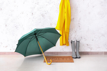 Stylish umbrella, raincoat and gumboots in hallway