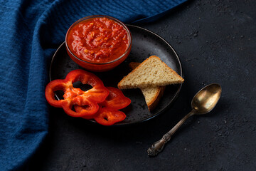Fresh Ajvar made from tomatoes and paprika on a black background. With slices of bread. Homemade aivar