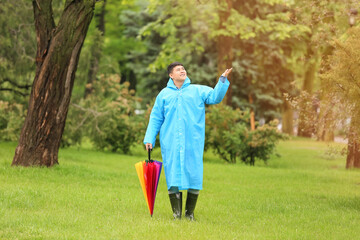 Young Asian man with umbrella wearing raincoat in park